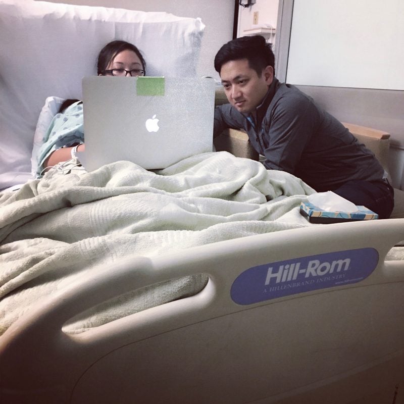 stephanie in hospital bed looking at laptop with husband